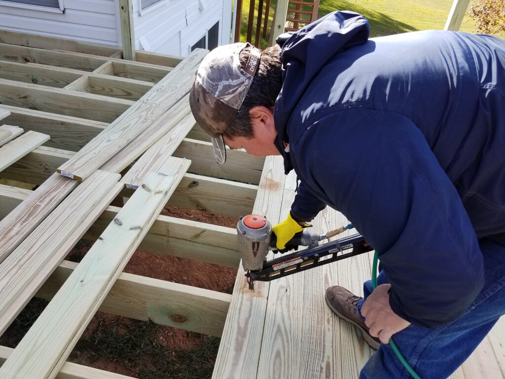 Deck restoration in progress with technician repairing wood planks and preparing surface for sealing